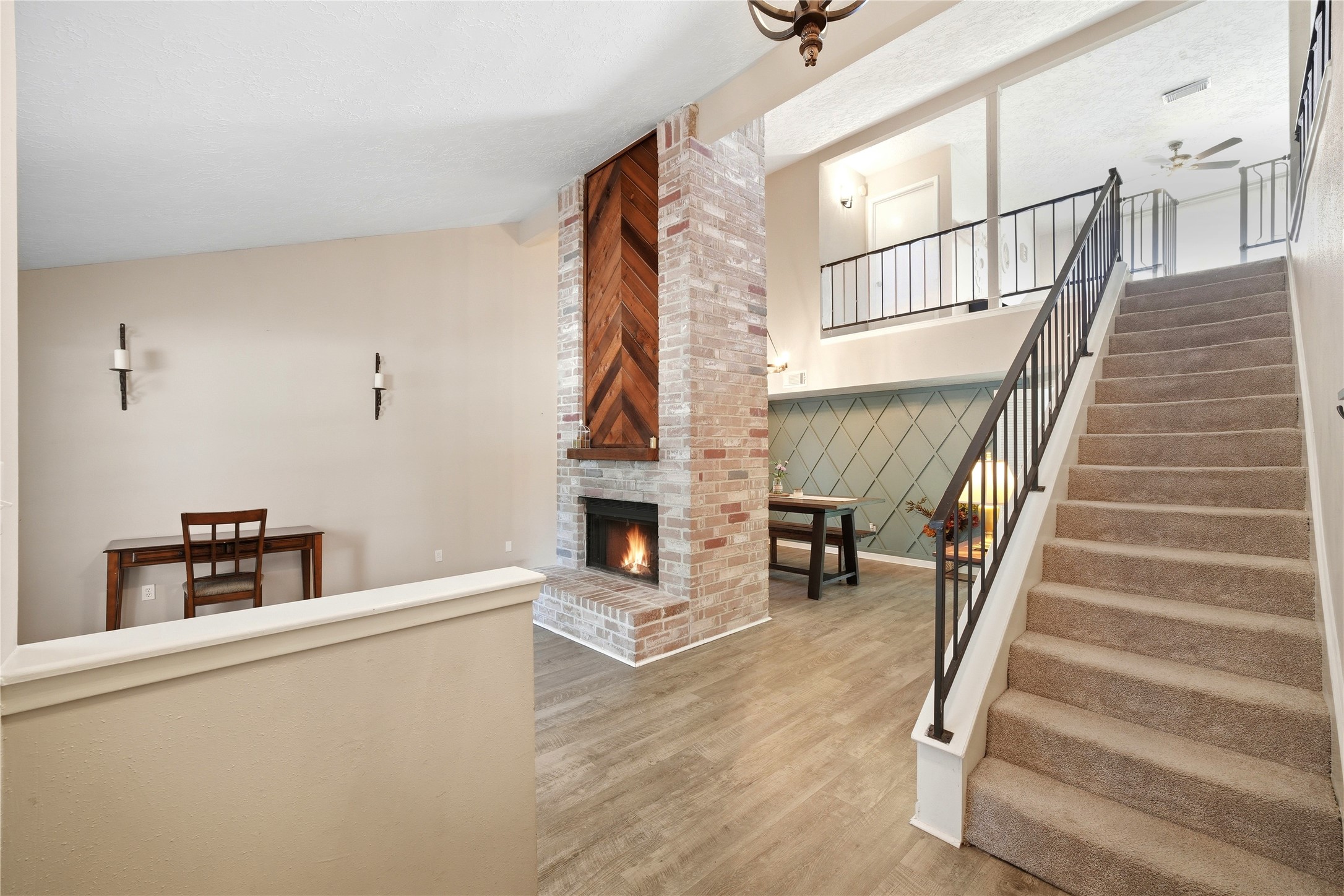 4718 Temple Bell Drive Spring, TX 77388 - Photo 7 of 50 This photo showcases a cozy living space featuring a brick fireplace with a wooden accent, an adjacent seating area, and a staircase with wrought iron railing leading to an upper level. The room has a warm, inviting feel with neutral tones and modern light fixtures.
