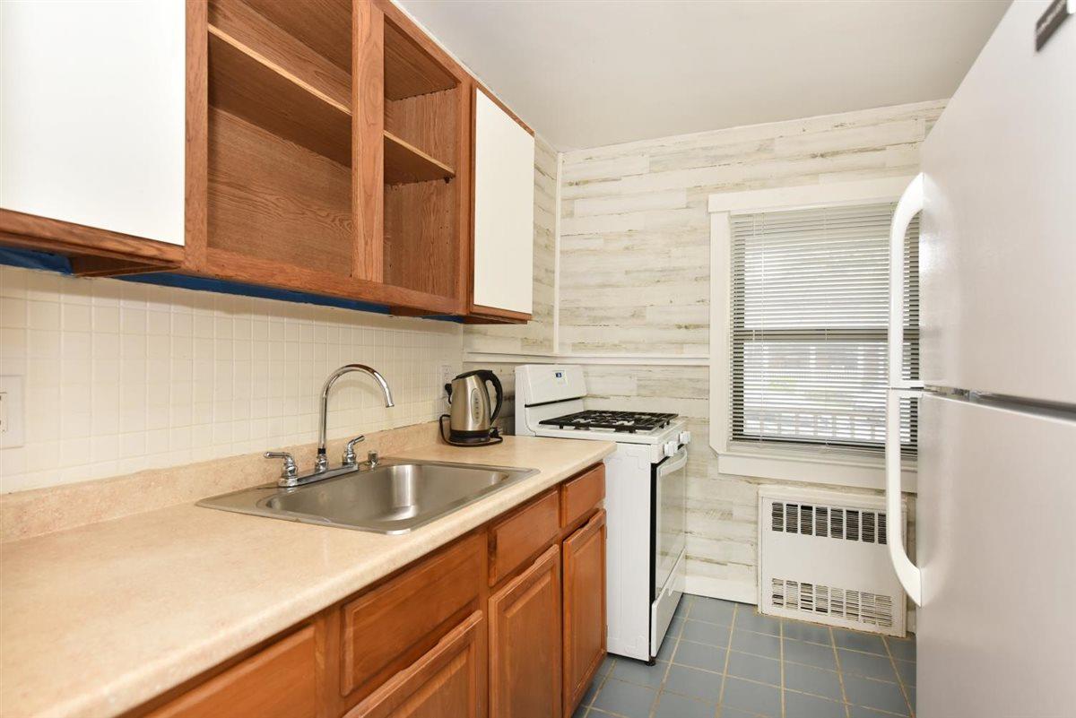 196-65 69th Avenue, Unit 1 Queens, NY 11365 - Photo 13 of 24 Kitchen with a sink, light countertops, white appliances, radiator, and dark tile patterned flooring