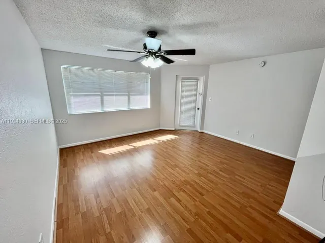 an empty room with wooden floor chandelier fan and windows