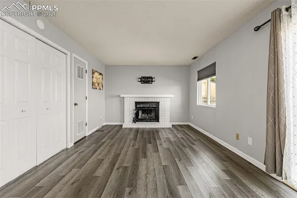 a view of an empty room with wooden floor fireplace and a window
