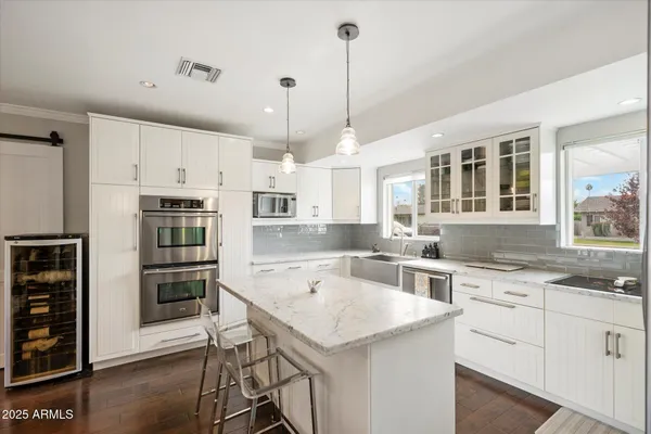 a kitchen with a stove a sink a kitchen island with chairs and white cabinets