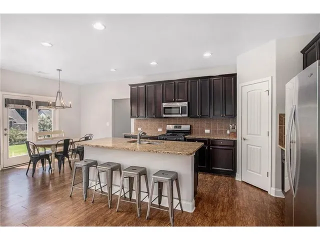 a kitchen with stainless steel appliances granite countertop a stove top oven a sink dishwasher a dining table and chairs with wooden floor