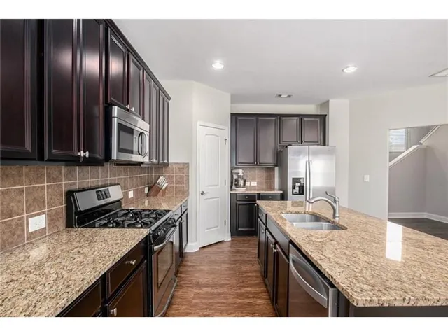 a kitchen with kitchen island granite countertop stainless steel appliances a sink stove refrigerator and cabinets