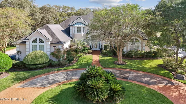 a view of a white house with a big yard plants and large trees