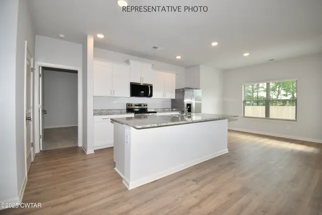 a kitchen with kitchen island granite countertop a stove top oven a sink a refrigerator and a microwave