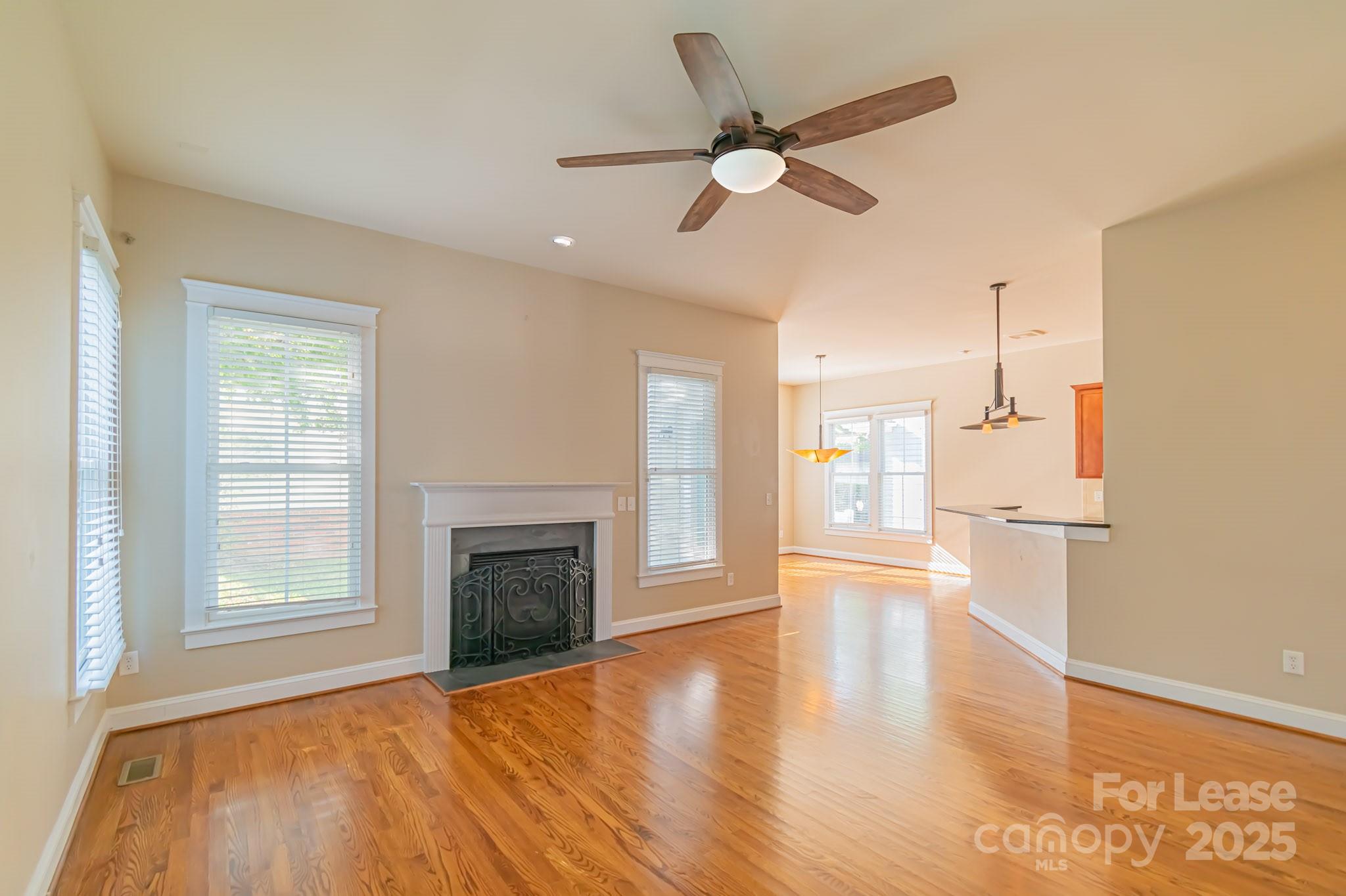 742 Revival Row Fort Mill, SC 29708 - Photo 10 of 32 an empty room with wooden floor a ceiling fan and a kitchen view
