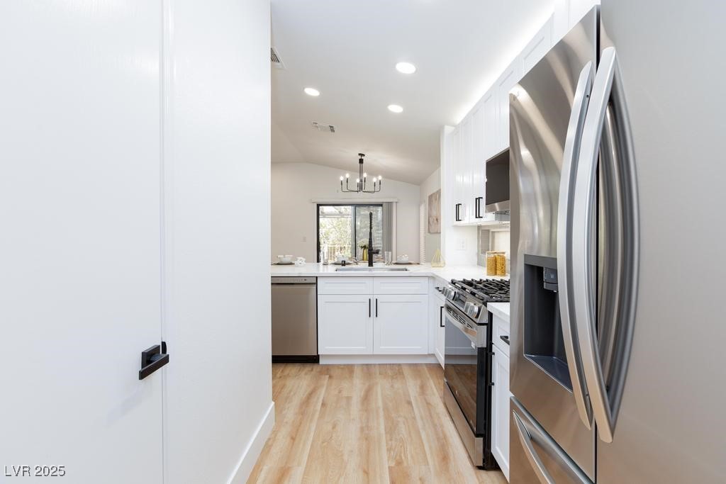 502 Edgefield Ridge Place Henderson, NV 89012 - Photo 10 of 38 Kitchen with stainless steel appliances, a sink, white cabinetry, light wood-type flooring, and a chandelier
