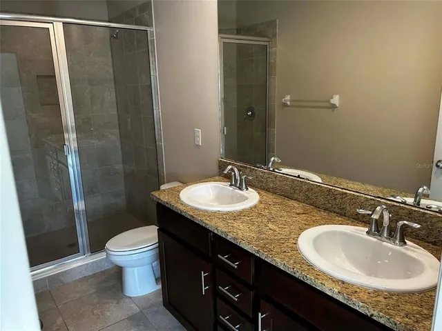 a bathroom with a granite countertop sink a toilet a mirror and shower