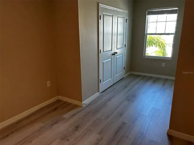 an empty room with wooden floor closet and windows