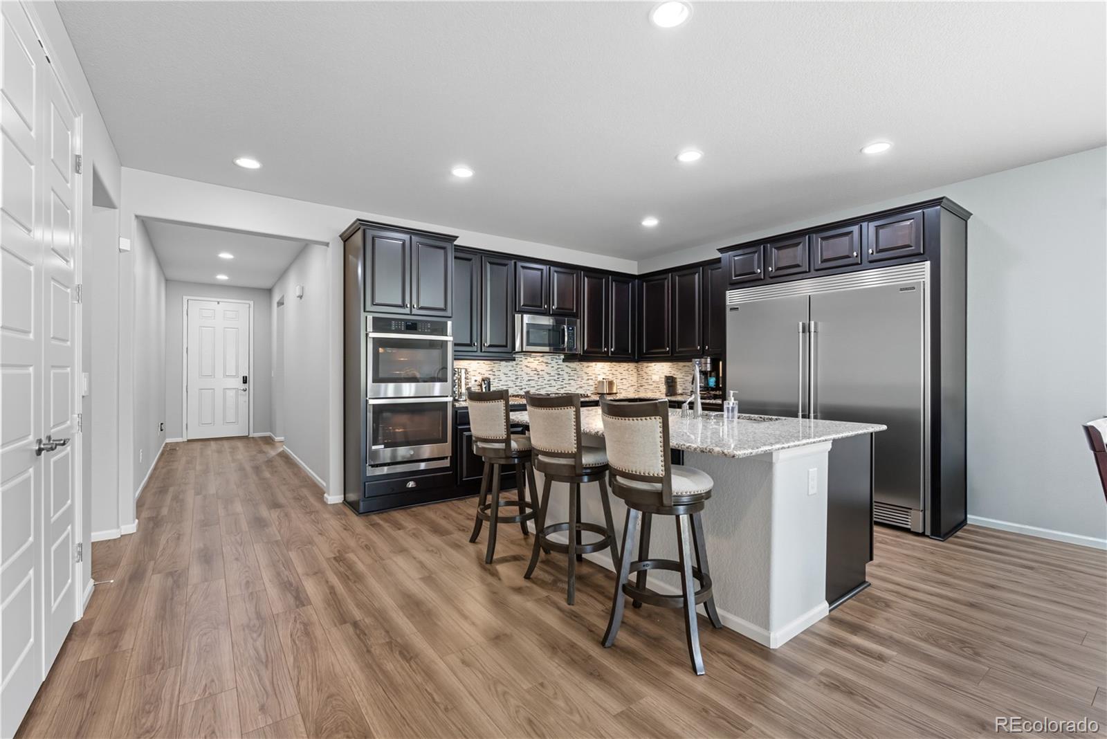 5740 Berry Ridge Wy. Castle Rock, CO 80104 - Photo 8 of 38 a kitchen with stainless steel appliances kitchen island granite countertop a table chairs and a refrigerator