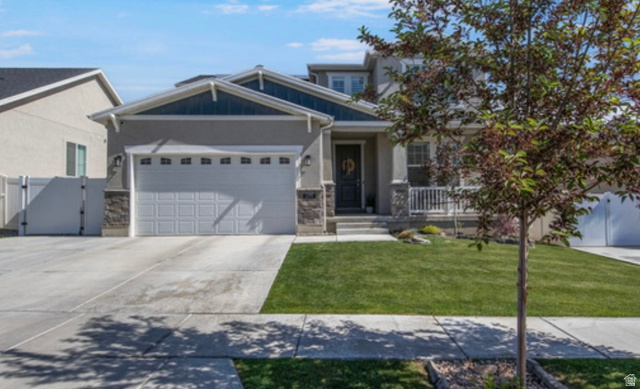 1295 East Granite Peak Road Eagle Mountain, UT 84005 - Photo 3 of 35 Contemporary stucco exterior with stone accents, a two-car garage, a covered front porch, and a lush green lawn