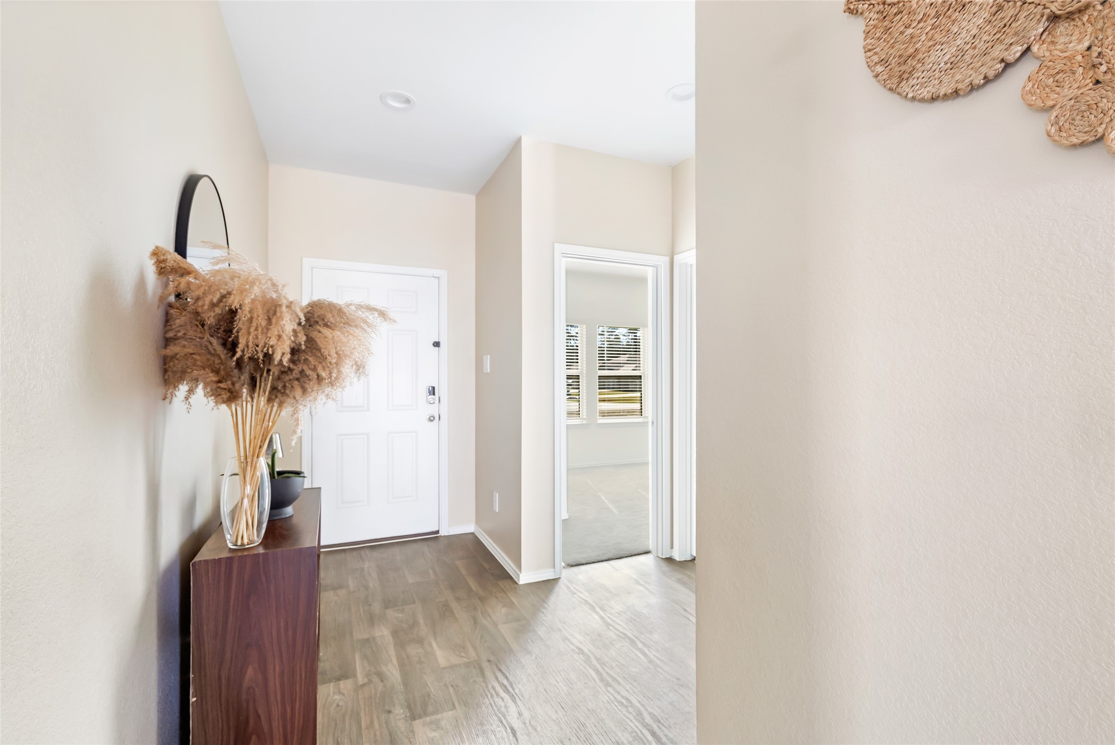 811 Republic Road New Caney, TX 77357 - Photo 15 of 37 This photo showcases a bright and welcoming entryway with light-colored walls and wood flooring. A modern console table with decorative vases adds charm, and the area leads to a well-lit adjacent room.