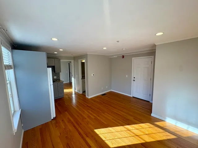 a view of empty room with wooden floor and kitchen