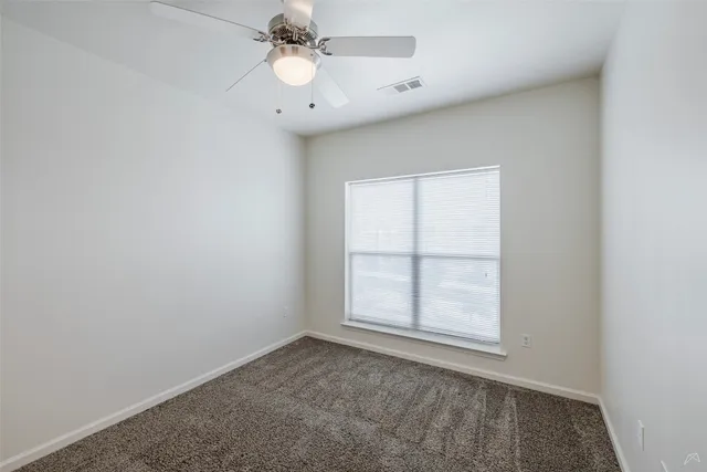 an empty room with wooden floor ceiling fan and window
