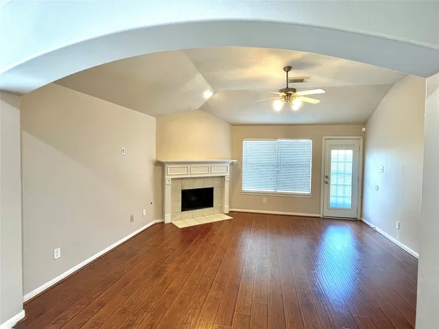 a view of an empty room with wooden floor fireplace and a window