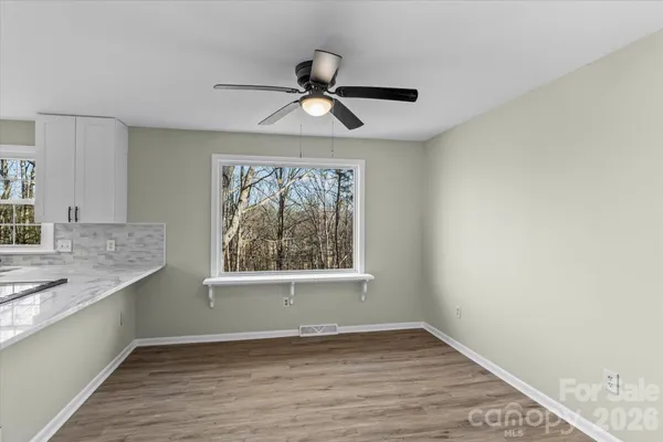 an empty room with wooden floor a ceiling fan and windows