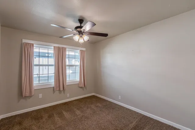 an empty room with chandelier fan and windows