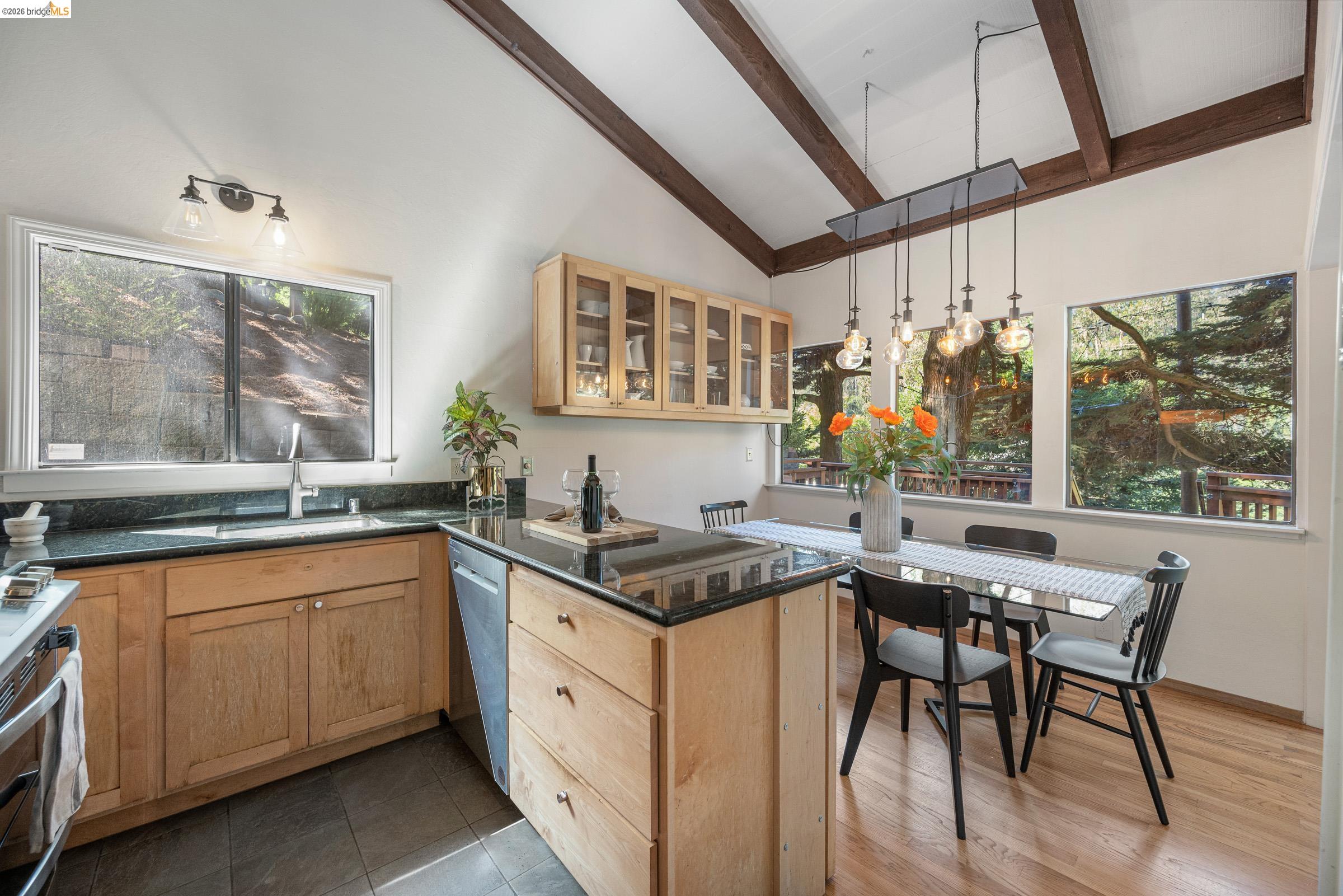 6600 Heather Ridge Way Oakland, CA 94611 - Photo 25 of 66 Kitchen and dining area featuring a vaulted ceiling with exposed wood beams, natural wood cabinetry, dark stone countertops, and wood-finish flooring