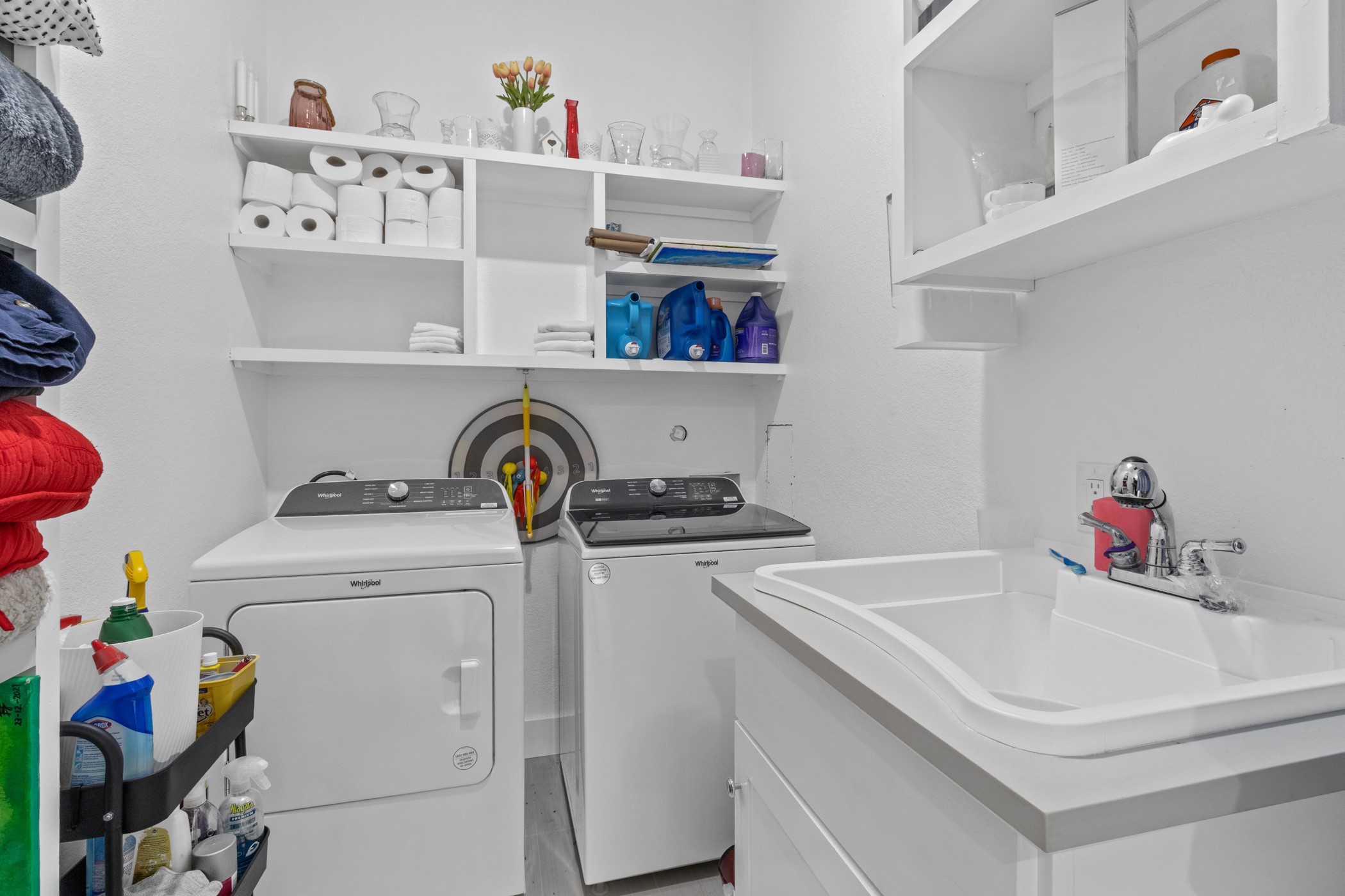 123 Zacate Street Elgin, TX 78621 - Photo 18 of 33 Dedicated laundry area featuring a utility sink with a chrome faucet, built-in cabinetry, white wall shelving, and durable flooring