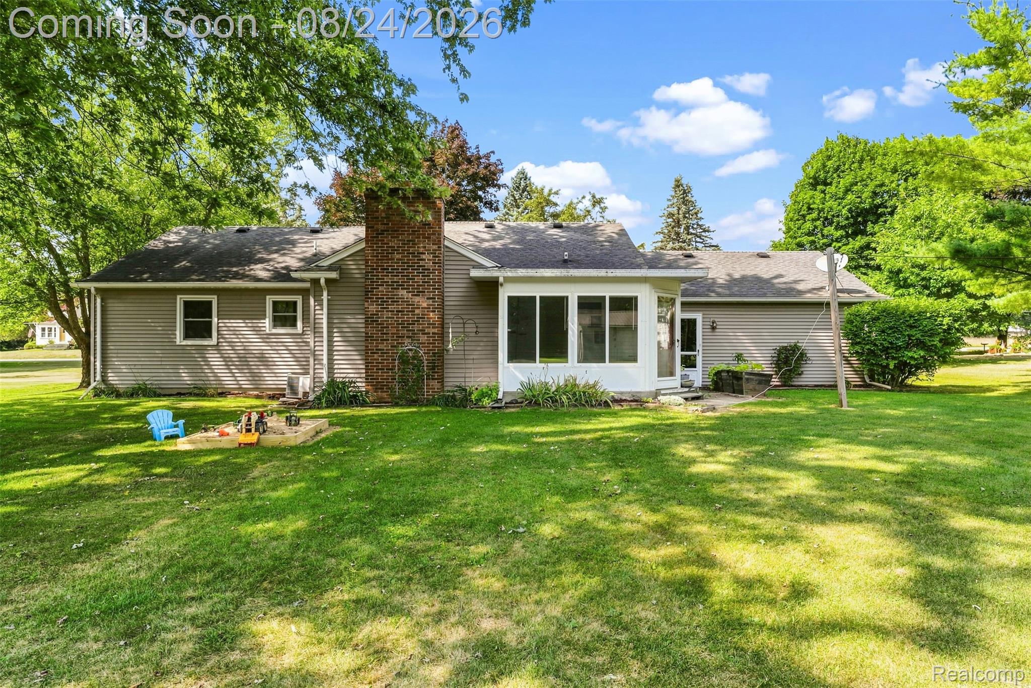 Expansive green yard with mature trees, a brick chimney, and an enclosed patio