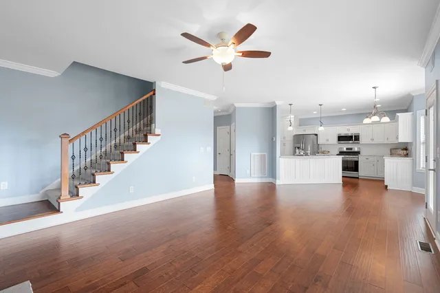 a view of an empty room with wooden floor and a kitchen