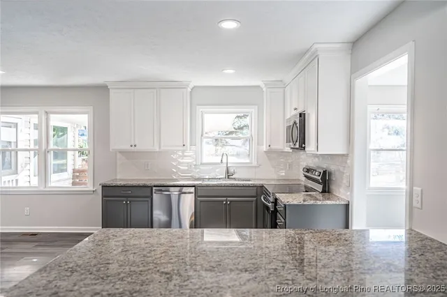 a large kitchen with stainless steel appliances granite countertop a sink and a white cabinets