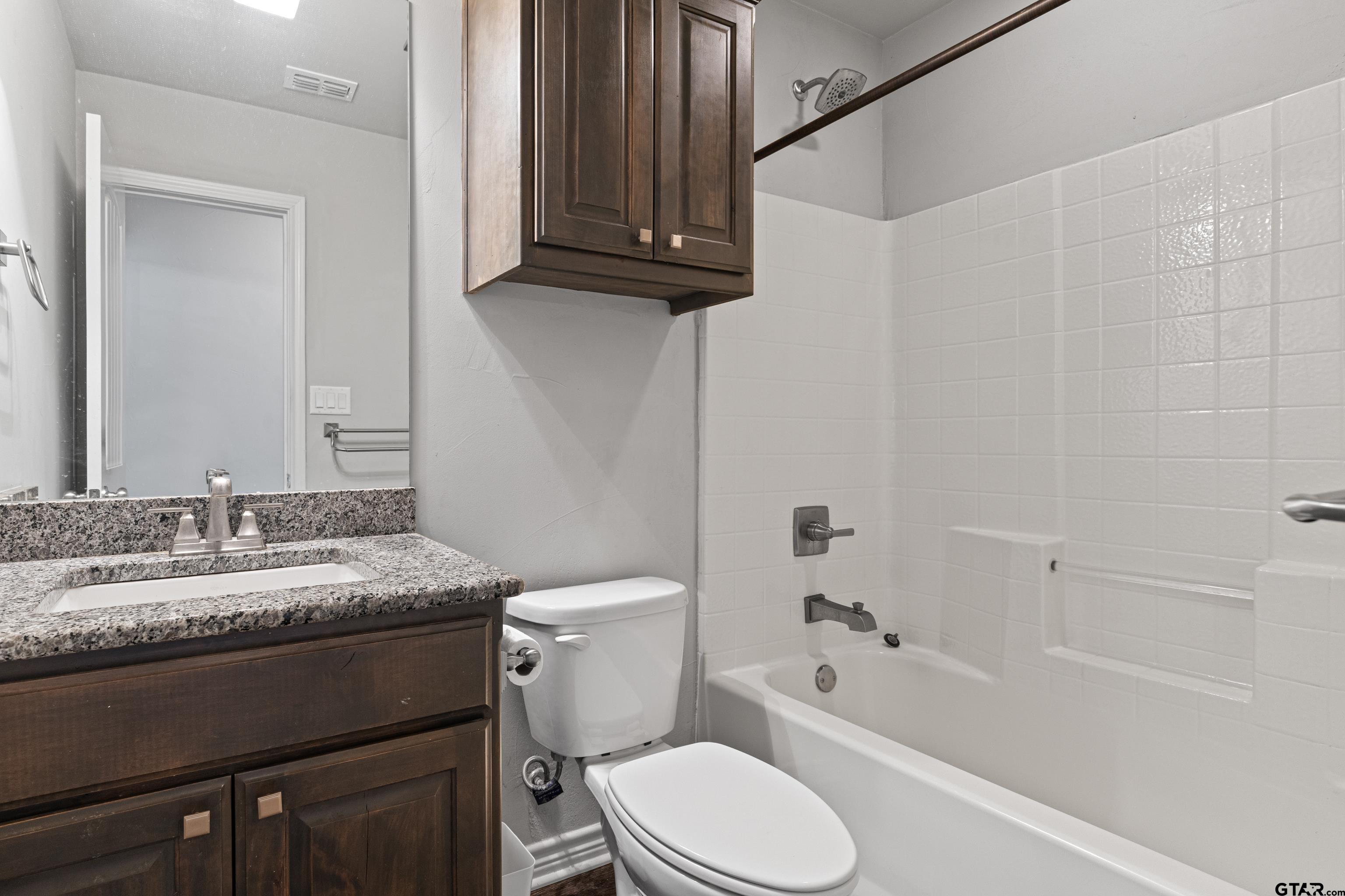 302 Collins Avenue Longview, TX 75605 - Photo 22 of 36 a bathroom with a granite countertop sink toilet a mirror and bathtub