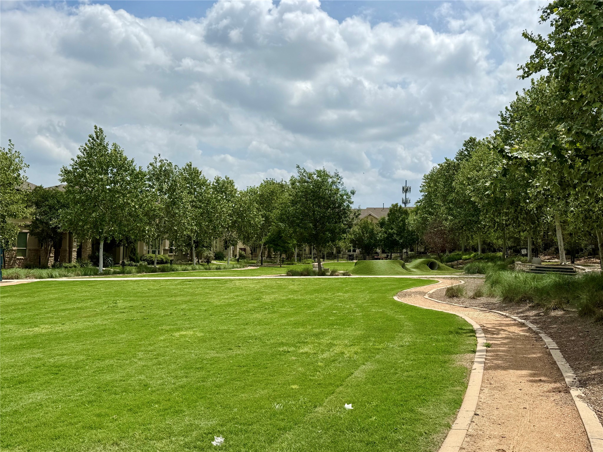 6814 East Riverside Drive, Unit 73 Austin, TX 78741 - Photo 31 of 33 Expansive green space featuring a manicured lawn, mature trees, a winding pathway, and residential architecture in the background