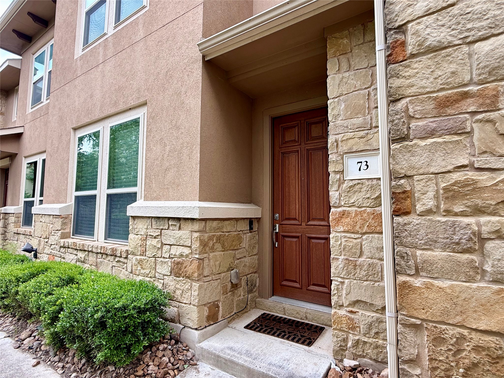 6814 East Riverside Drive, Unit 73 Austin, TX 78741 - Photo 4 of 33 Stucco facade with stone accent detailing, featuring a panel-design entry door, multiple windows, and ground-level landscaping
