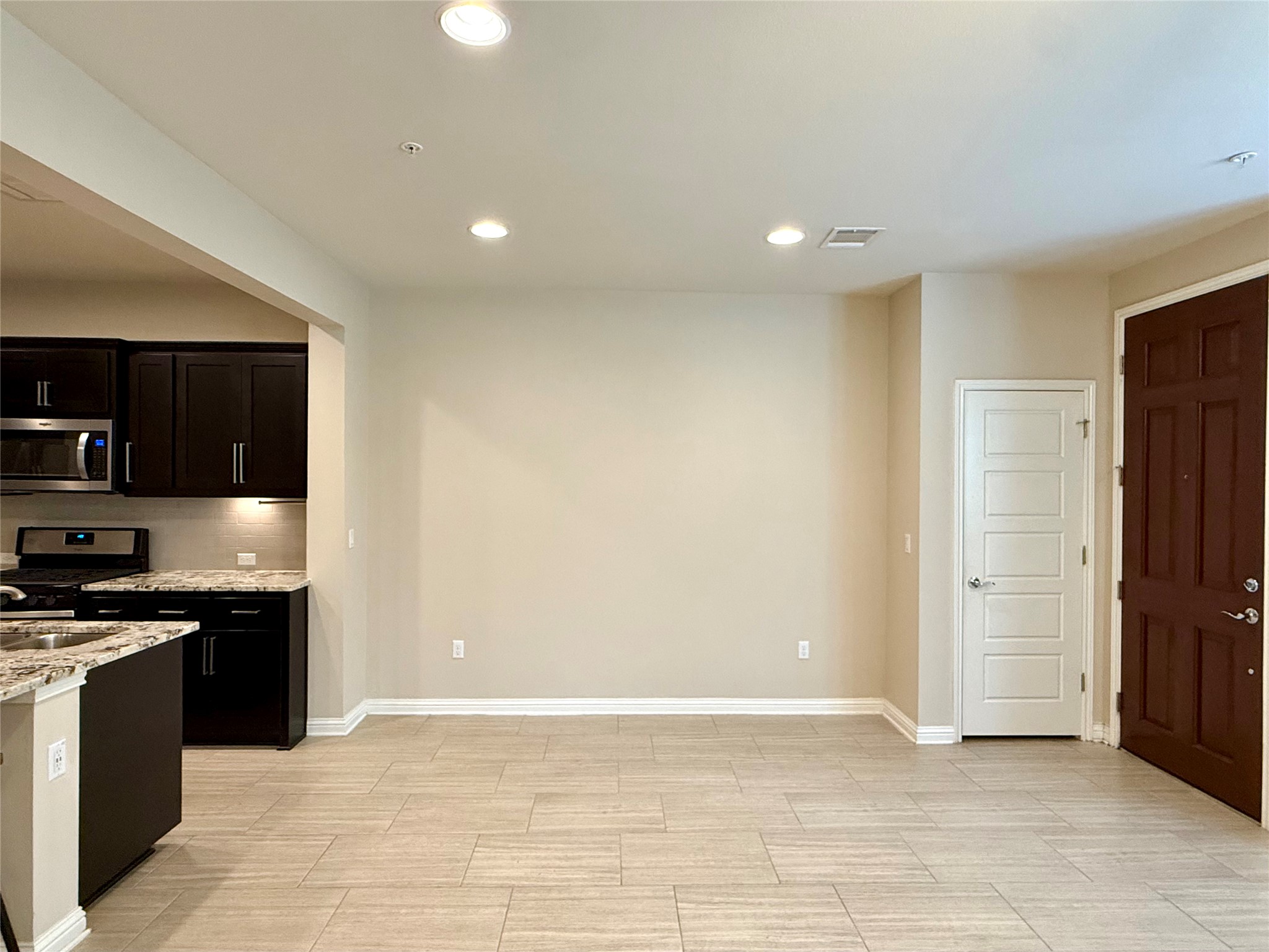 6814 East Riverside Drive, Unit 73 Austin, TX 78741 - Photo 6 of 33 Open-concept living area featuring light-toned tile flooring, recessed lighting, and a kitchen with dark wood-finish cabinetry, light-toned countertops, and stainless steel appliances