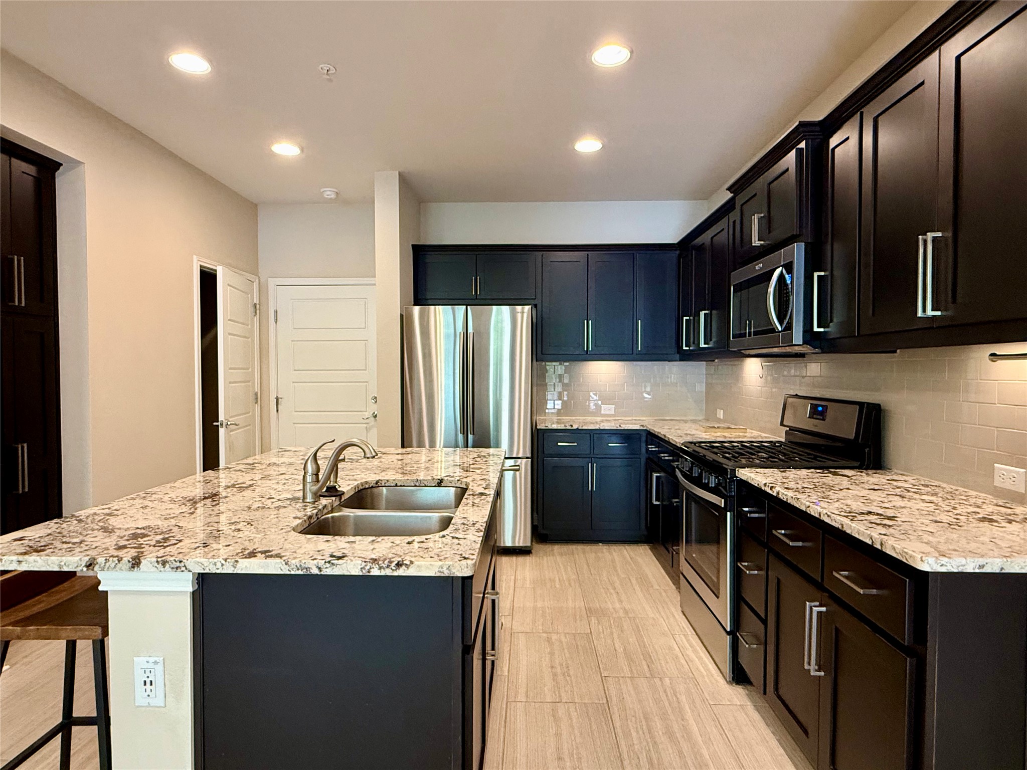6814 East Riverside Drive, Unit 73 Austin, TX 78741 - Photo 9 of 33 Kitchen featuring a large island with an undermount double sink, granite countertops, dark wood cabinetry, stainless steel appliances, and tile flooring