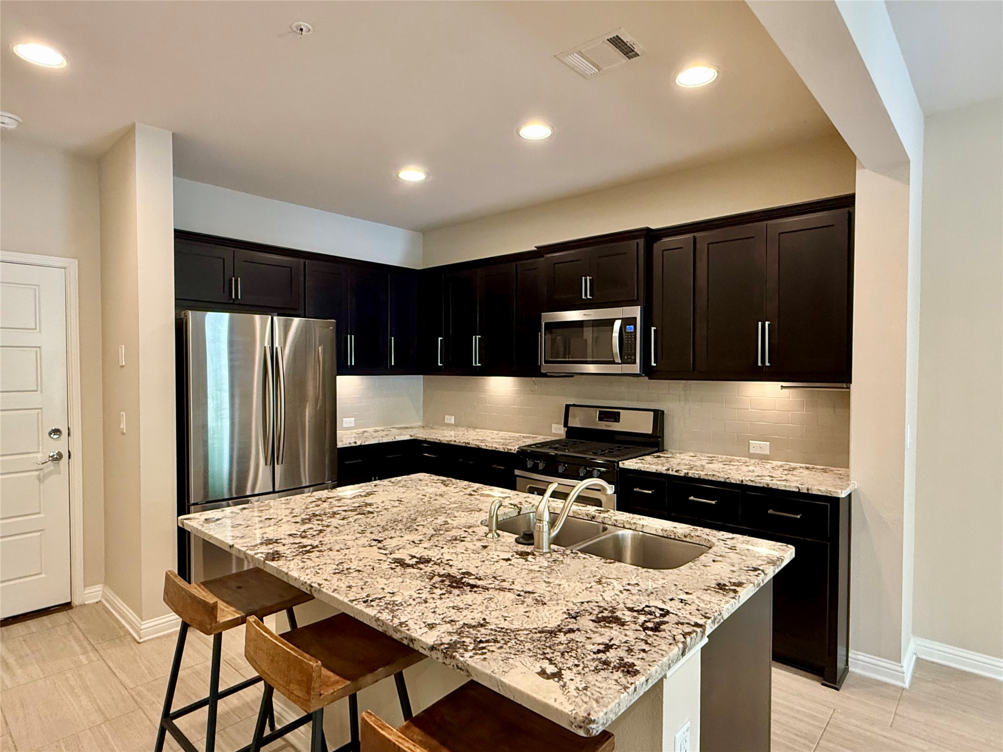 6814 East Riverside Drive, Unit 73 Austin, TX 78741 - Photo 10 of 33 Gourmet kitchen with dark wood-finish cabinetry, stainless steel appliances, and an expansive granite-top island with an undermount dual-basin sink