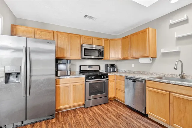 a kitchen with stainless steel appliances granite countertop a stove a sink dishwasher a refrigerator and a microwave oven with wooden floor