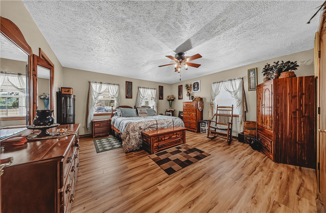 21587 West Hickory Flat Road Springdale, AR 72764 - Photo 24 of 45 Large primary bedroom with multiple windows, ceiling fan, wood flooring, and ample space for substantial furniture.