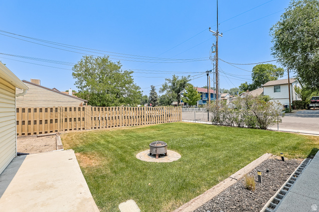 59 East 8680th Street South Sandy, UT 84070 - Photo 28 of 33 Fenced backyard with a central fire pit, concrete patio, and a landscaped border