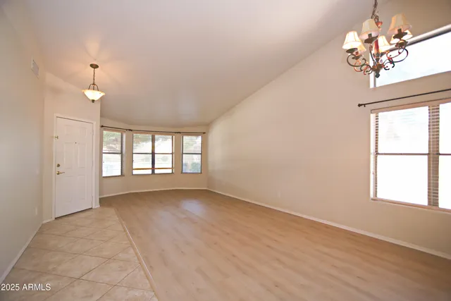 an empty room with chandelier fan and windows