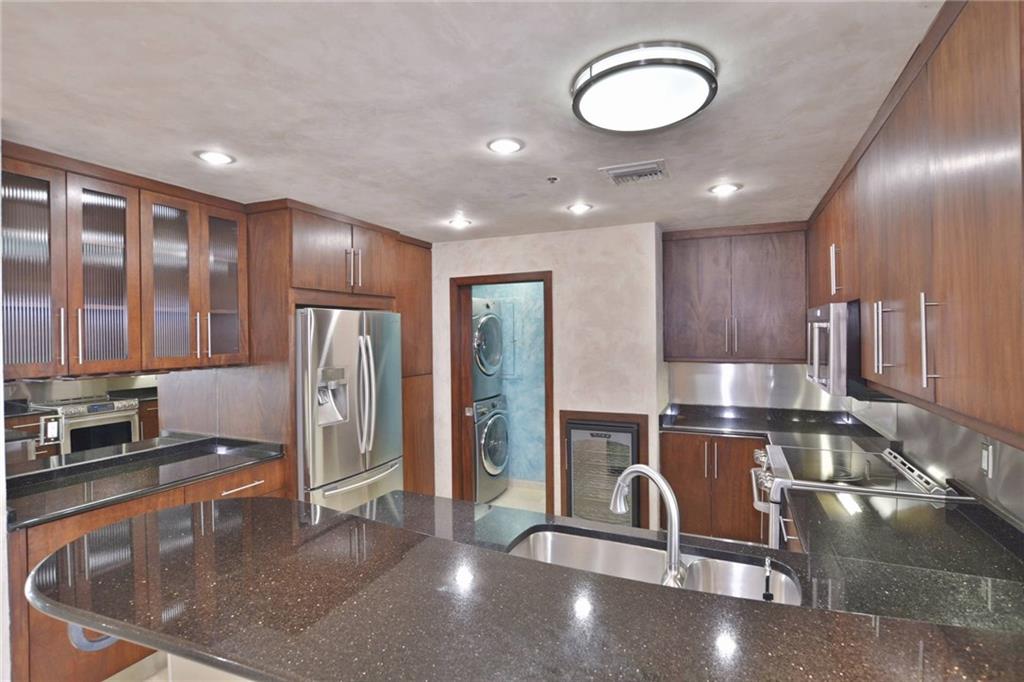 40 North Interstate Highway 35, Unit 12C2 Austin, TX 78701 - Photo 7 of 21 Kitchen with stainless steel appliances, stacked washer / dryer, dark stone countertops, glass fronted cabinets, and a peninsula