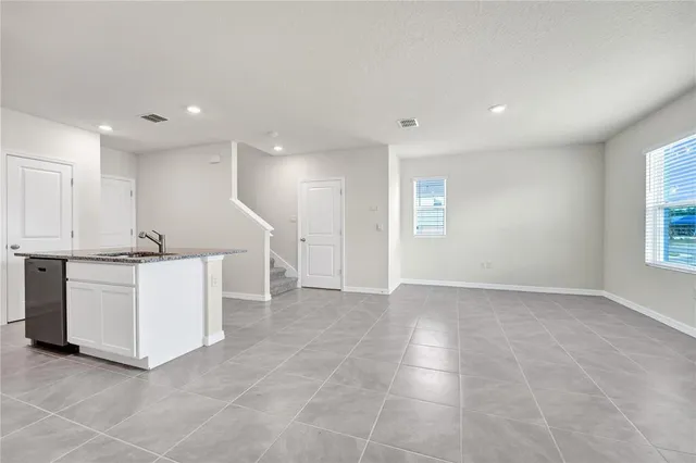 a view of an empty room with kitchen and window
