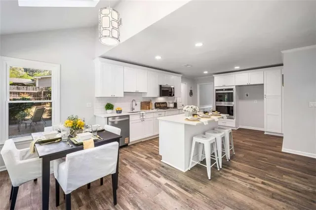 a kitchen with stainless steel appliances granite countertop a sink a stove a dining table and chairs