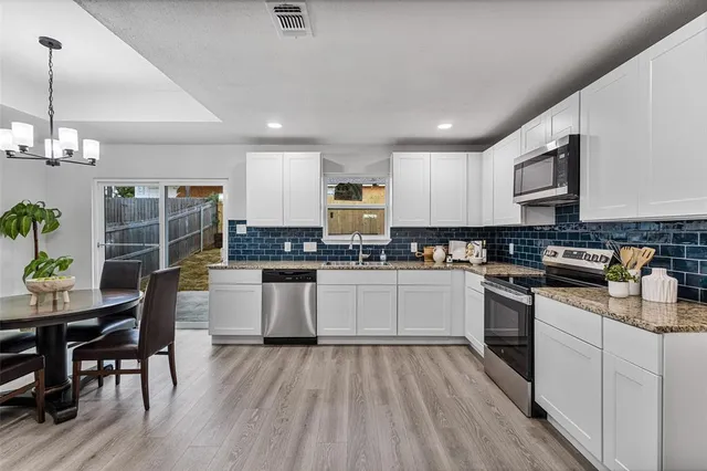 a kitchen with granite countertop wooden floors stainless steel appliances and white cabinets