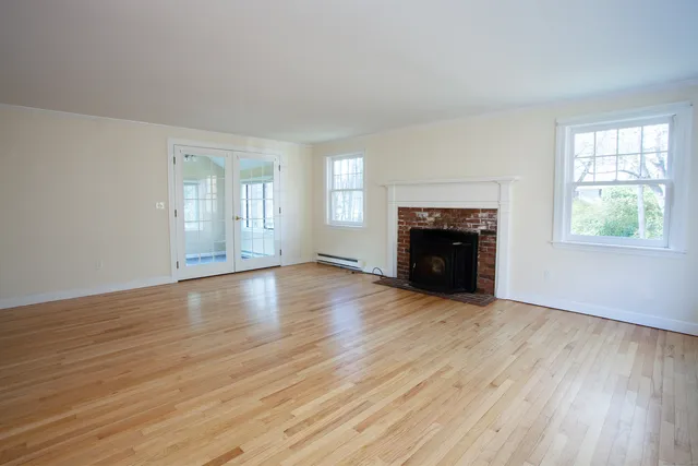 an empty room with wooden floor fireplace and windows