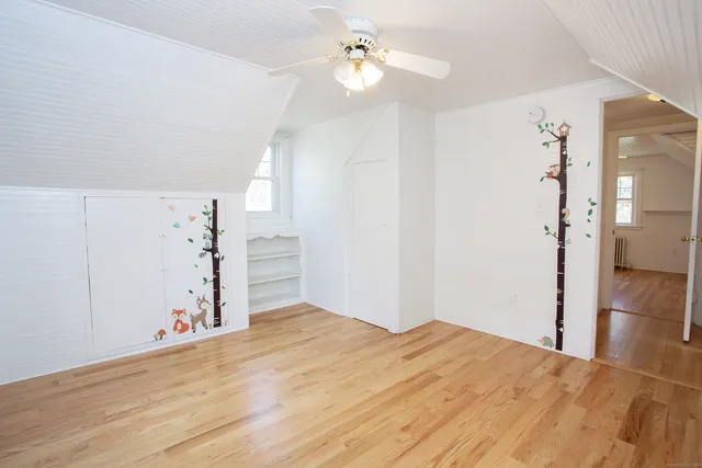 an empty room with wooden floor chandelier fan and windows