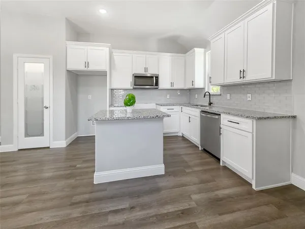 a kitchen with stainless steel appliances granite countertop a stove top oven a sink and white cabinets