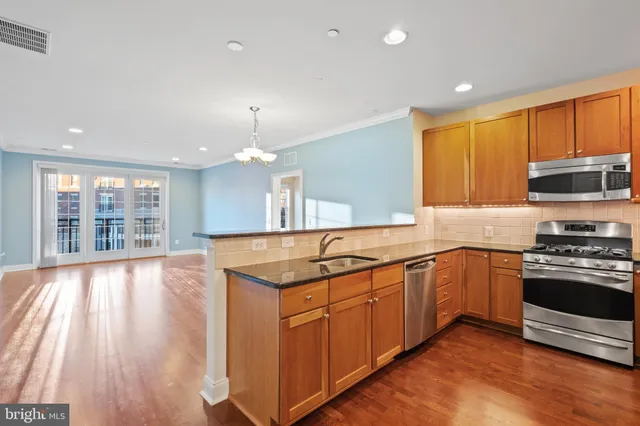 a kitchen with stainless steel appliances granite countertop hardwood floor sink stove and wooden cabinets