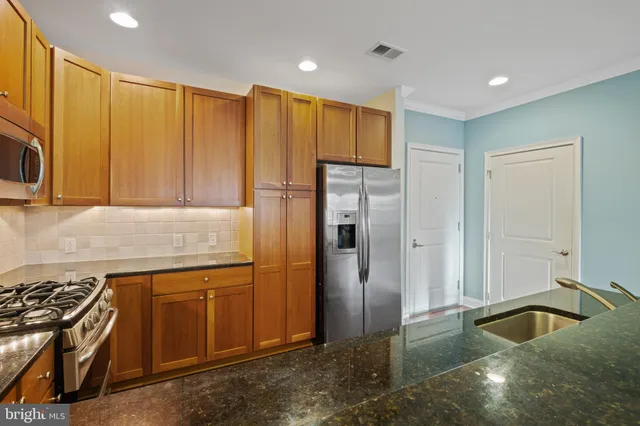 a kitchen with stainless steel appliances granite countertop a refrigerator a sink and a stove with wooden floor