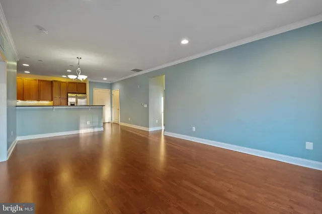 an empty room with wooden floor and kitchen view