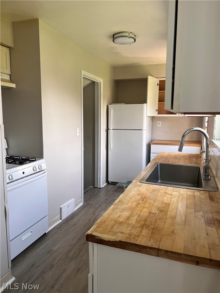 16350 Rockside Road Maple Heights, OH 44137 - Photo 11 of 34 Kitchen featuring butcher block countertops, wood-finish flooring, white cabinetry, a stainless steel sink with a gooseneck faucet, and a white refrigerator