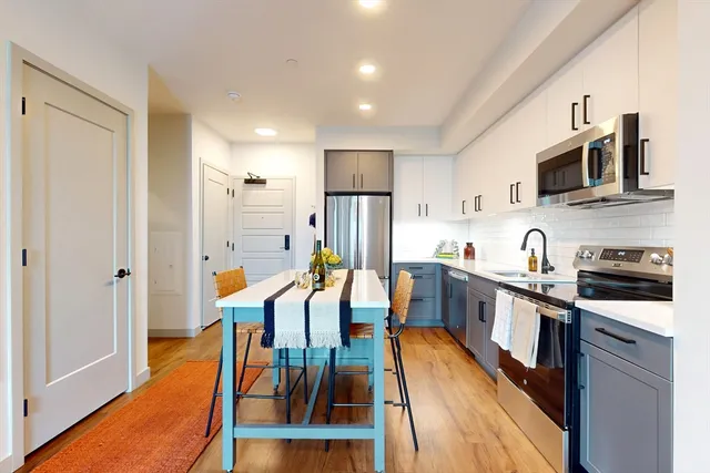 a kitchen with stainless steel appliances granite countertop a refrigerator a stove top oven a sink dishwasher and white cabinets with wooden floor