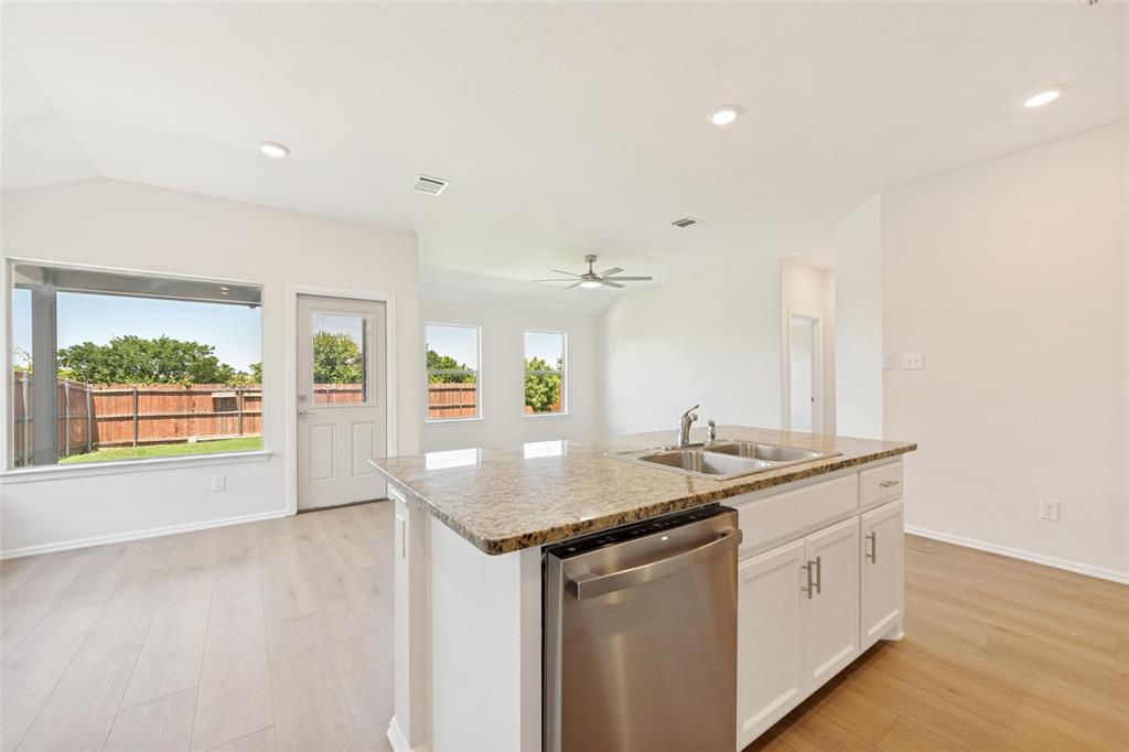 857 Watson Way Crowley, TX 76036 - Photo 6 of 25 Kitchen island with dual stainless steel sink, stainless steel dishwasher, white cabinetry, and a light-toned stone countertop