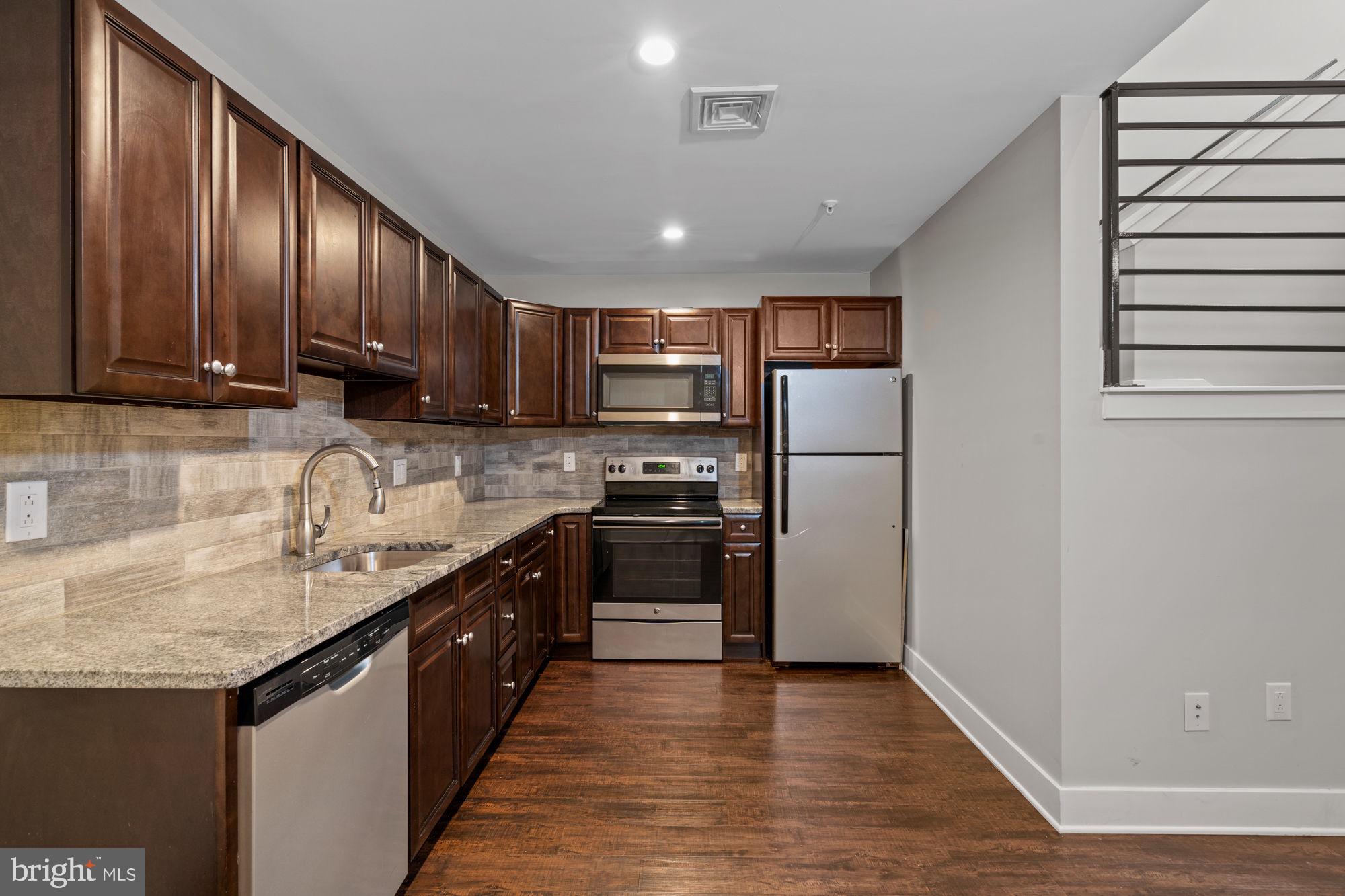 a kitchen with stainless steel appliances granite countertop a refrigerator a sink dishwasher a stove and a microwave oven on granite countertops